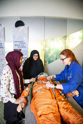 Science Communicator explains how a spacesuit works to two visitors