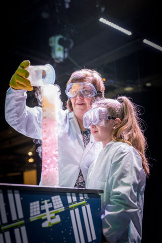 Woman and child in white coats and PPE take part in a chemistry demonstration 