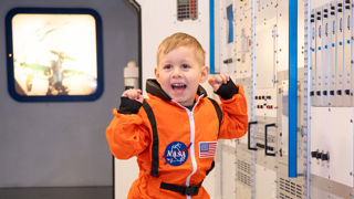Small boy in an orange spacesuit in the Columbus Module at Small Space Day