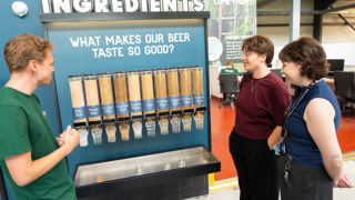 Isaac, Eilish and Kat looking at a panel listing the ingredients of beer.  The caption says "what makes our beer taste so good?"