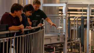 Eilish, Kat and Isaac looking down over Everard's beer brewing process