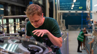 Isaac leaning over a beer brewing machine and explaining the process