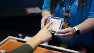 A hand points at a piece of fabric in a glass cube being held by a Presenter