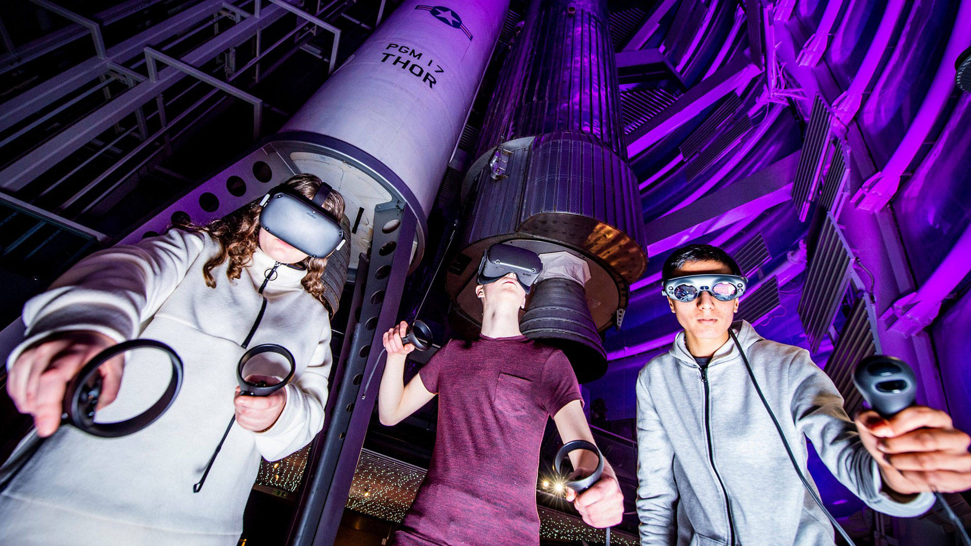 Three teens with VR headsets under the rockets
