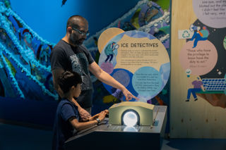 Two People Interact With Ice Detectives Exhibit