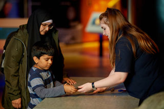 Child and Mother in hijab learning about meteorites from a science communicator